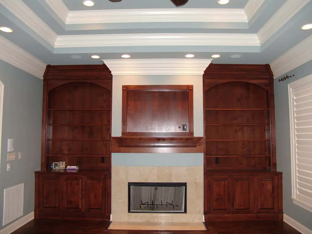 A residential living room with a painted trey ceiling and stained built-in bookshelves beside the fireplace