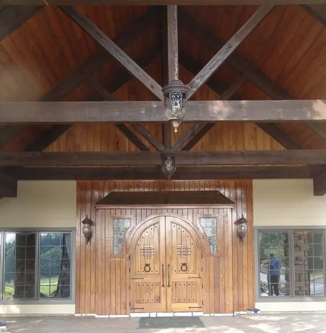 A stained wood porte-cochere entrance with a worker reflected in the window glass