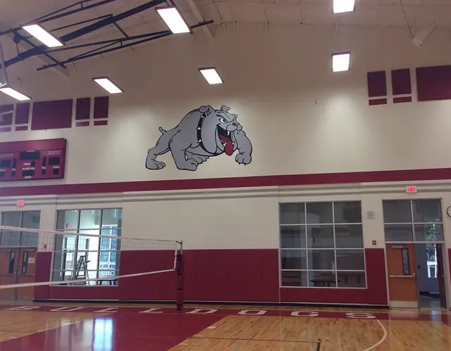 A school gymnasium wall with a painted Jasper Bulldogs mural, a ladder still standing against the wall